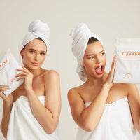 Two models holding the microfibre hair towels in their biodegradable pacakging
